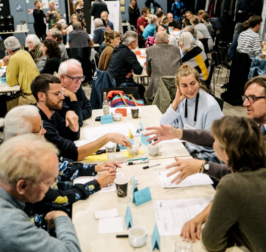 Mange borgere til møde, sidder og diskuterer rundt om borde